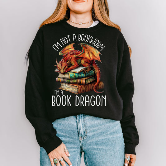 The book dragon sweatshirt has a design of a sleeping dragon on top of stacked books. The text says, "I'm not a bookworm. I'm a book dragon."
The model is wearing the colour black.