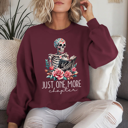 The just one more chapter sweatshirt has a design of a skeleton reading a book. A funny joke amongst book lovers. Because we cannot put down a good book.
The model is wearing the colour maroon.